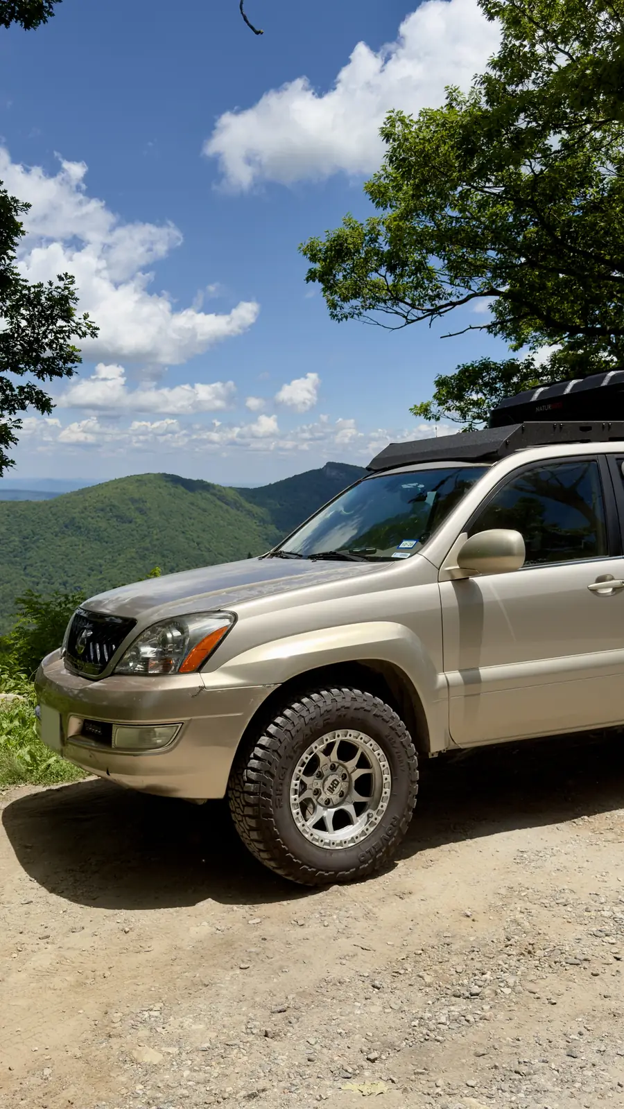 Ginny, a tan 2003 GX470 with a roof box and all-terrain tires, parked on a mountain overlook